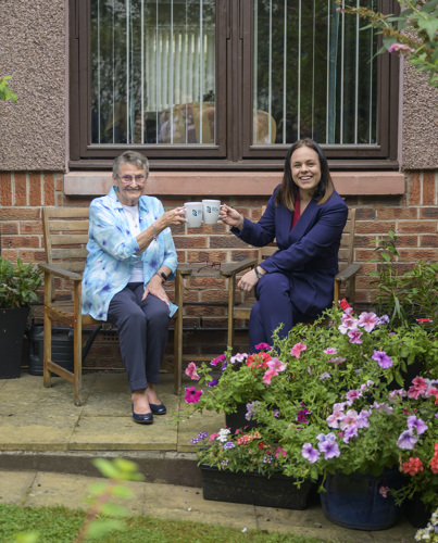 Muriel Allison and Deputy First Minister, Kate Forbes sitting on chairs outside Muriel's house touching their mugs