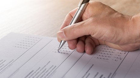 A pen in hand filling out a paper questionnaire