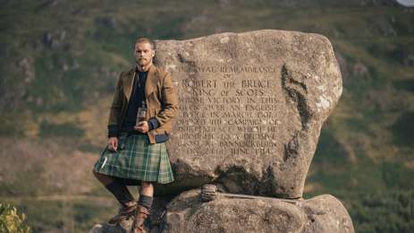 Sam Heughan standing against rock 