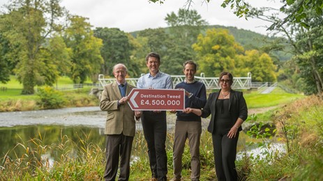 Tweed Forum and SOSE representatives holding a £4.5m sign in front of River Tweed