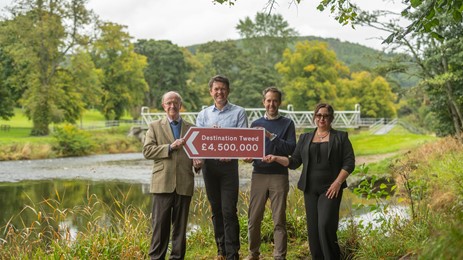 Tweed Forum and SOSE representatives holding a £4.5m sign in front of River Tweed